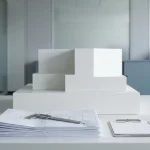 Geometrisch wit architectuurmodel op bureau met technische tekeningen, schuifmaat en checklist in minimalistisch kantoor
