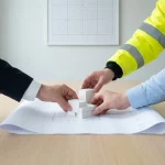 Architecten en bouwteam plaatsen wit massingmodel op blauwdruk op vergadertafel, minimalistische setting met zacht daglicht
