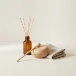 Minimalistische productfoto met amber diffuserflesje, houten klankblok met mallet en linnen stof op matte tafel, zacht daglicht