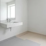 Minimalistische badkamerhoek met wastafel, brede spiegel en RVS steunbeugel, antislipvloerovergang en neutrale tinten