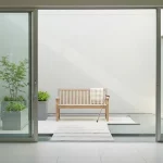 Houten bank met plaid en wandelstok in minimalistische binnentuin van verpleeghuis, met plantenbakken en waterpartij