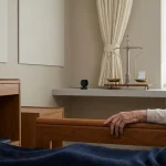 Hand van oudere op bedrail in rustige dementiezorgkamer, met discrete camera en privacyweegschaal met keycard
