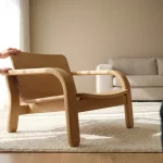 Stevige houten kinderstoel in minimalistische woonkamer, kinderhand op armleuning en volwassen hand steunt rugleuning.