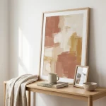 Ingelijste abstracte kunst boven eikenhouten consoletafel met boek, mok, fotolijst en linnen plaid in zacht ochtendlicht