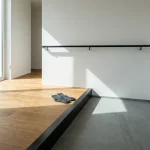 Minimalistische halhoek met trede tussen houten vloer en stenen tegel, contrastrand, zwarte leuning en sokken bij de rand
