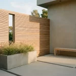 Minimalistische patio met houten lamellenwand, bank en plantenbak met siergrassen, betontegels en golden-hour licht
