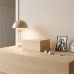 Houten herinneringsdoos op minimalistisch nachtkastje met bril, familiefoto, huissleutel, klok en lamp in zacht licht