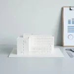 Matwit ziekenhuisgebouwmodel op bureau naast dashboard-clipboard, caliper en liniaal, minimalistisch in zacht daglicht
