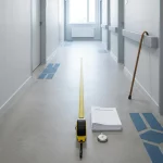 Grote meetlat op vloer in minimalistische ziekenhuisgang met formulieren, stopwatch en wandelstok, symmetrisch daglicht