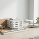 Architectenmaquette zorggebouw met huiskamerhoek en weegschaal met documenten en plant op natuurstenen tafel, minimalistisch