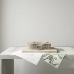 Schaalmodel zorggebouw op minimalistisch bureau met bouwplan en organische welzijnskaart, zacht daglicht en neutrale tinten