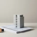 Modern appartementgebouw model met papierformulieren en rubberstempel op bureau, suggestie van lopende administratie onzekerheid