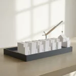 Minimalistisch architectuurmodel van witte rijtjeshuizen op een antraciet magazijnbasis, met kraanarm op betonnen tafel