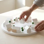 Handen plaatsen laatste miniatuurhuis in witte architectuurmaquette van cirkelvormige buurt rond gedeelde binnenplaats