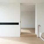 Toegankelijke deuropening met drempelloze doorgang, matte zwarte leuning, wandelstok bij bank, minimalistisch interieur in daglicht