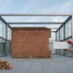 Historische bakstenen gevel met nieuw glazen stalen frame, architect plaatst modelblok op minimalistisch plein