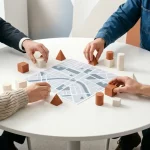 Ronde vergadertafel met stadskaart en bouwblokken; vier handen plaatsen stukken, teamwork in modern kantoordaglicht