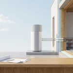 Moderne lucht-water warmtepomp met geïsoleerde leidingen naar nieuwbouwwand en vloerverwarming, bouwtekening op aanrecht