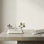 Witte weegschaal met munten en houten modern gebouwmodel op architectenbureau met blauwdrukken, minimalistisch design